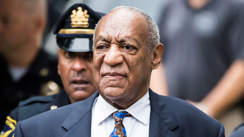 Bill Cosby en un juzgado con un policía detrás