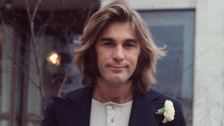 Dennis Wilson sonriendo con chaqueta en una fotografía posada