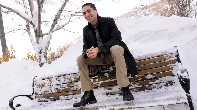 Nev Schulman sentado en un banco cubierto de nieve