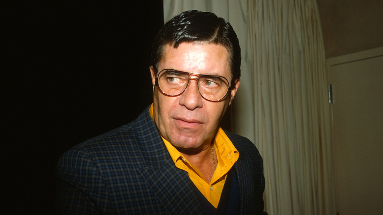 Jerry Lewis con gafas en un escenario con cortinas de fondo