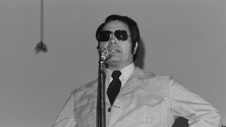 Jim Jones con gafas de aviador hablando en un micrófono
