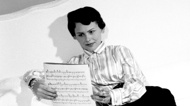 Joan Weber leyendo partituras en una cama blanca