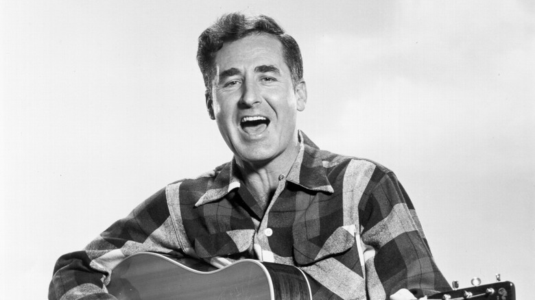 Sheb Wooley cantando y tocando guitarra en camisa a cuadros