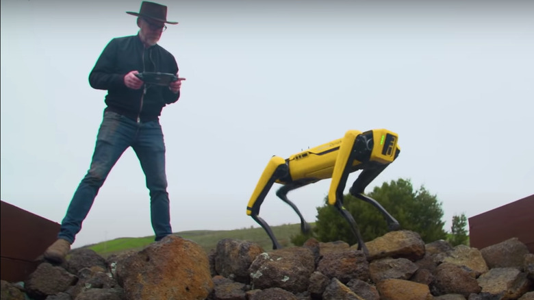 Adam Savage con un perro robot amarillo en manos y con controlador