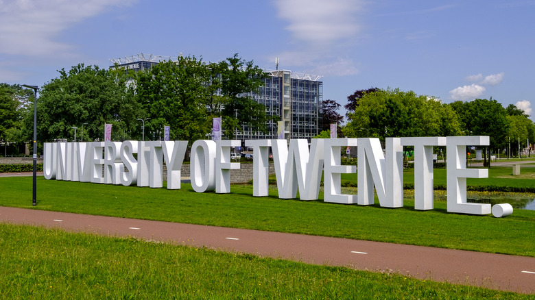 Vista exterior de la Universidad de Twente con letras blancas grandes en la hierba
