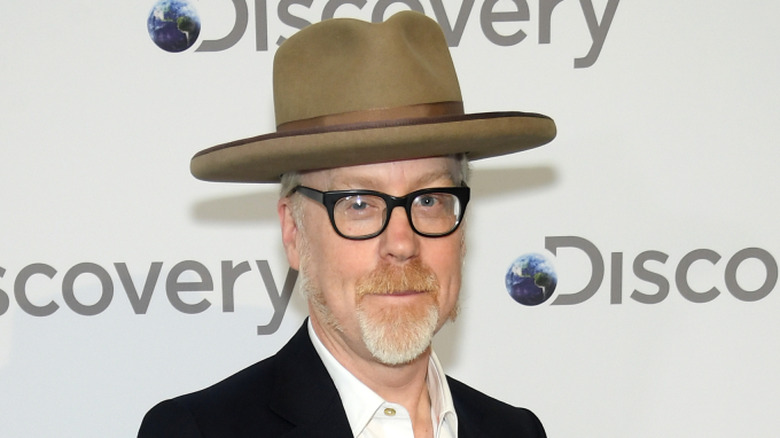 Adam Savage con barba de chivo, gafas, sombrero y traje en un evento de Discovery