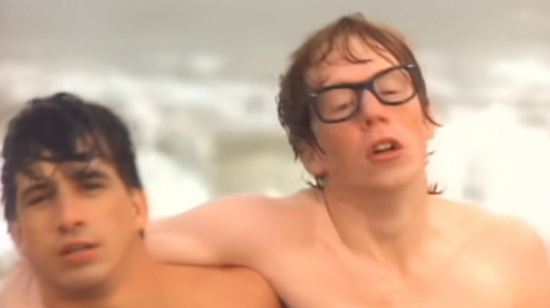 Adam Savage sin camiseta con gafas ayudado a salir del agua en un video de Billy Joel